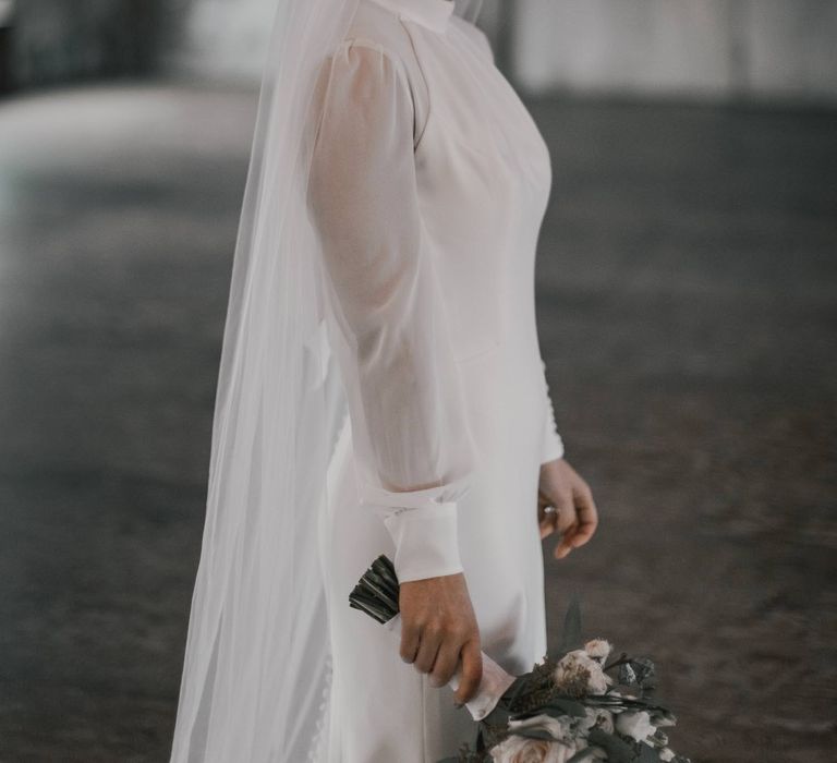 Bride looks at camera wearing classic white bridal gown and floor-length veil