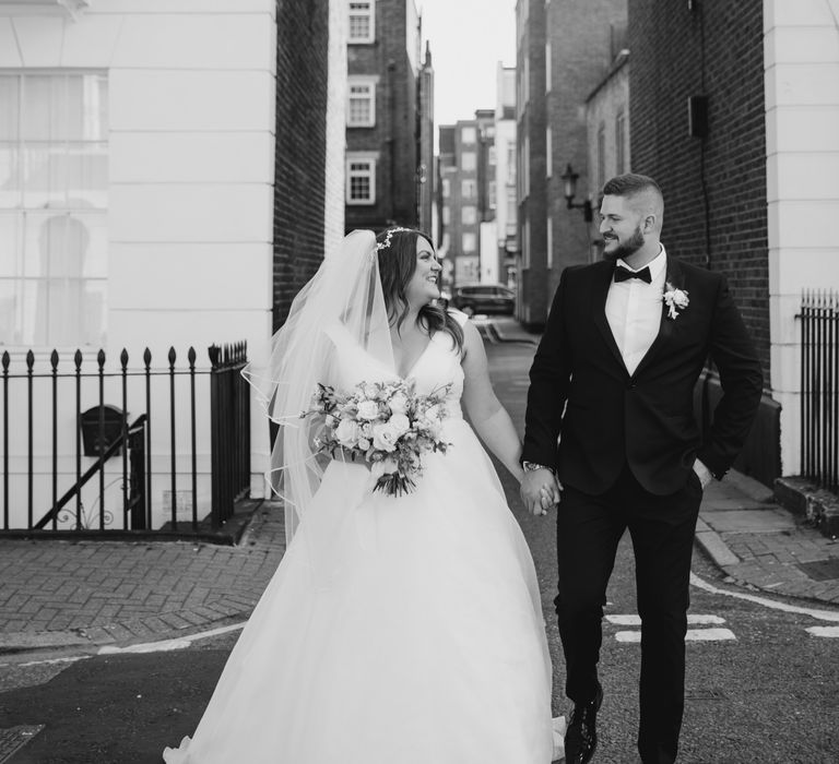 Black & white image of bride & groom walking through the streets of London on their wedding day