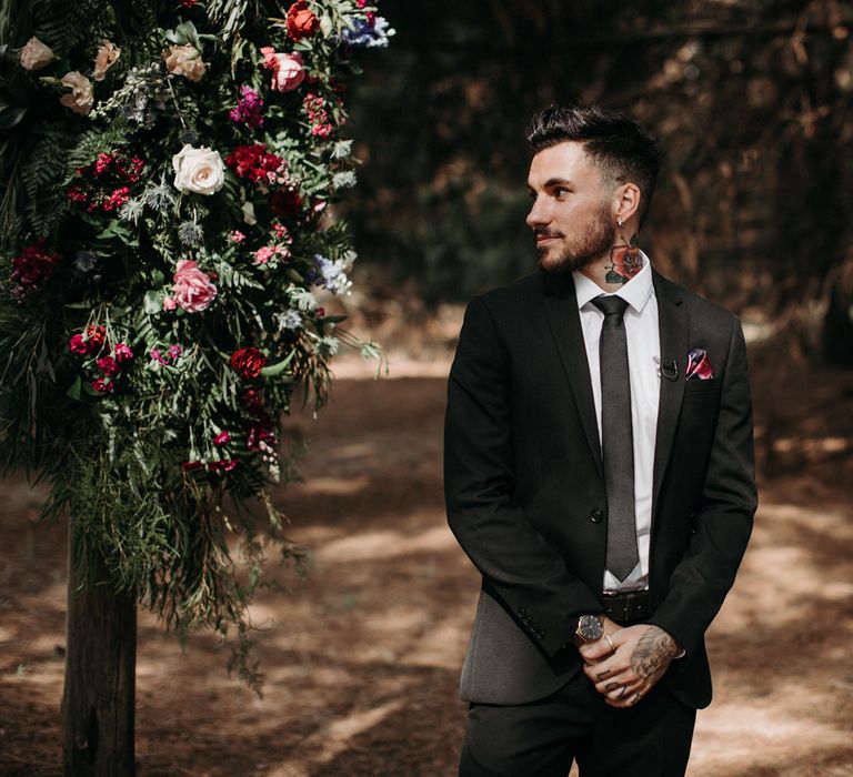 Groom with tattoos waiting at the altar of his outdoor rustic wedding