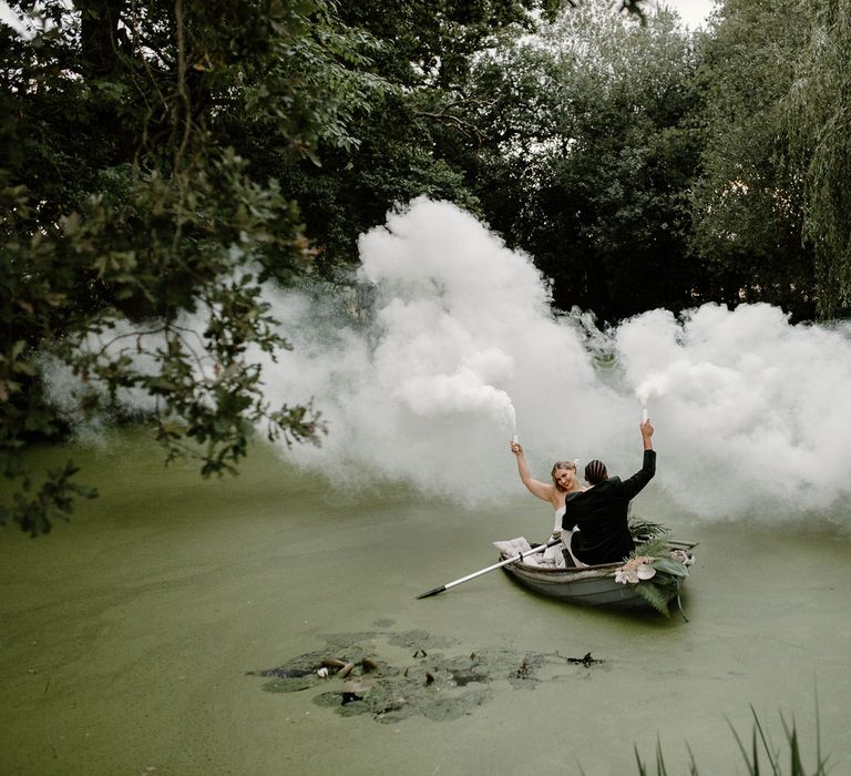 Bride and groom letting off white smoke bombs on a green lake for tropical wedding theme