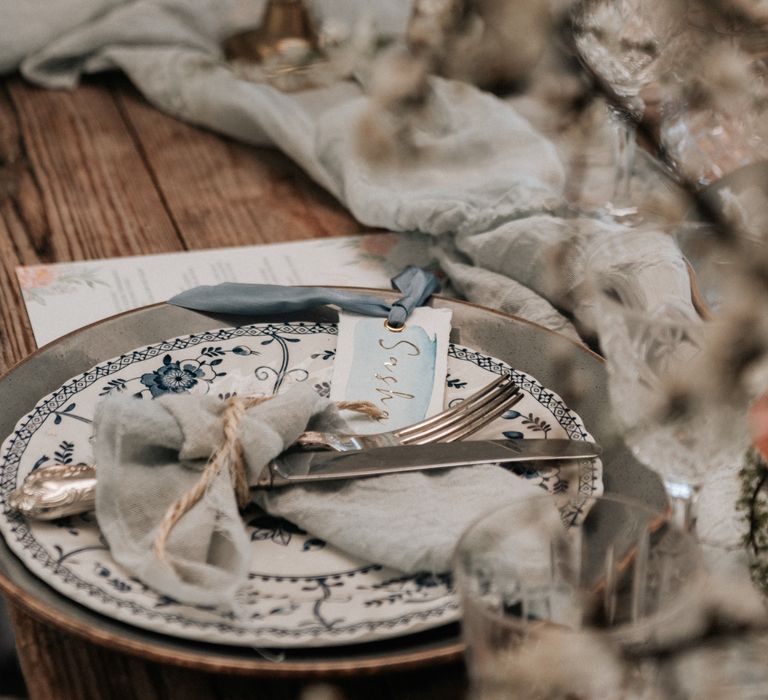 Pale grey plates with floral pattern, and pale blue napkins tied with brown string