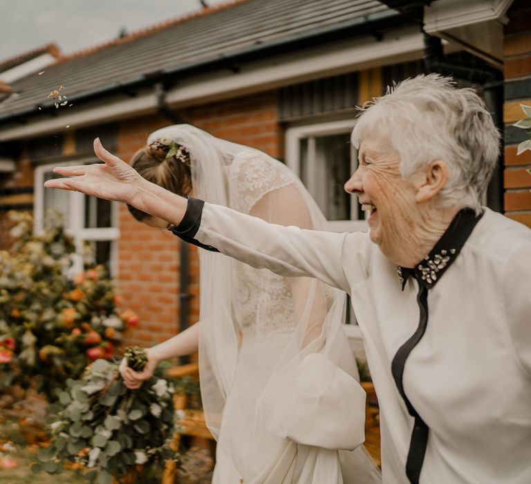 Smiling elderly wedding guest throws confetti next to bride in lace top with capped sleeves, satin skirt and veil after Dunluce Castle wedding