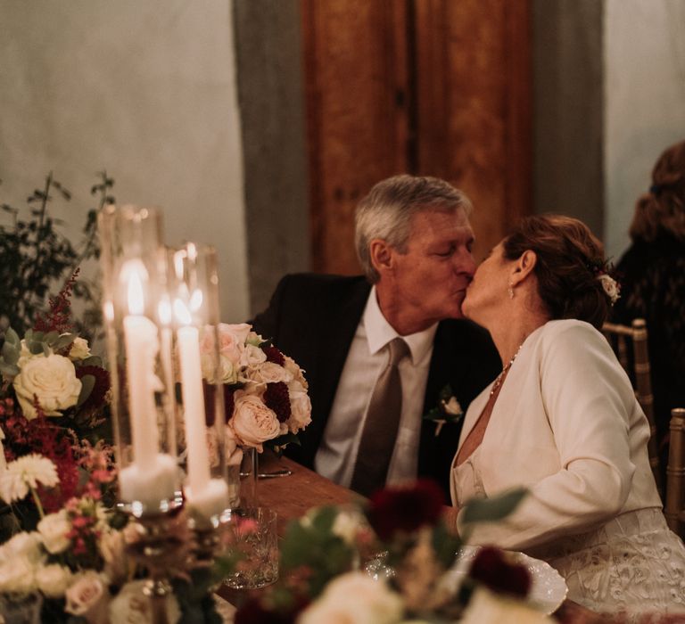 Bride & groom kiss as they sit down during wedding reception dinner