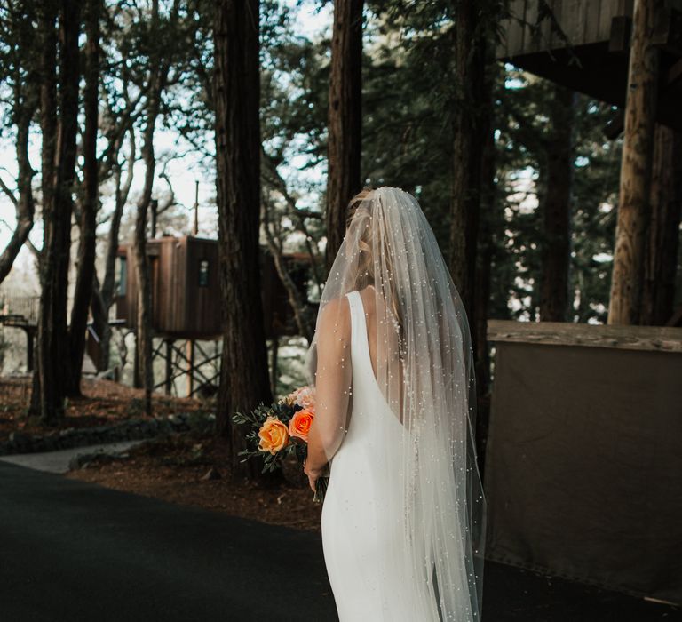 Bride walks along the road as she carries peach bouquet and wears pearl veil