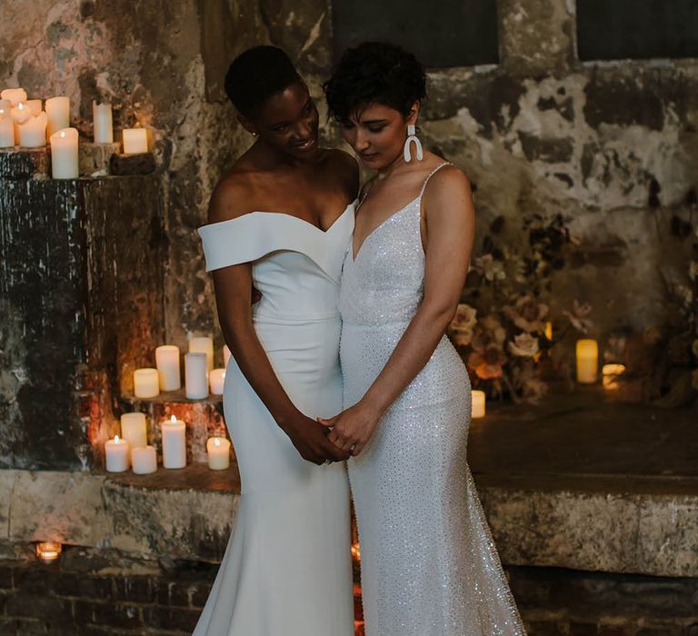 Two brides standing at the altar of The Asylum wedding venue with pillar candle wedding decor 