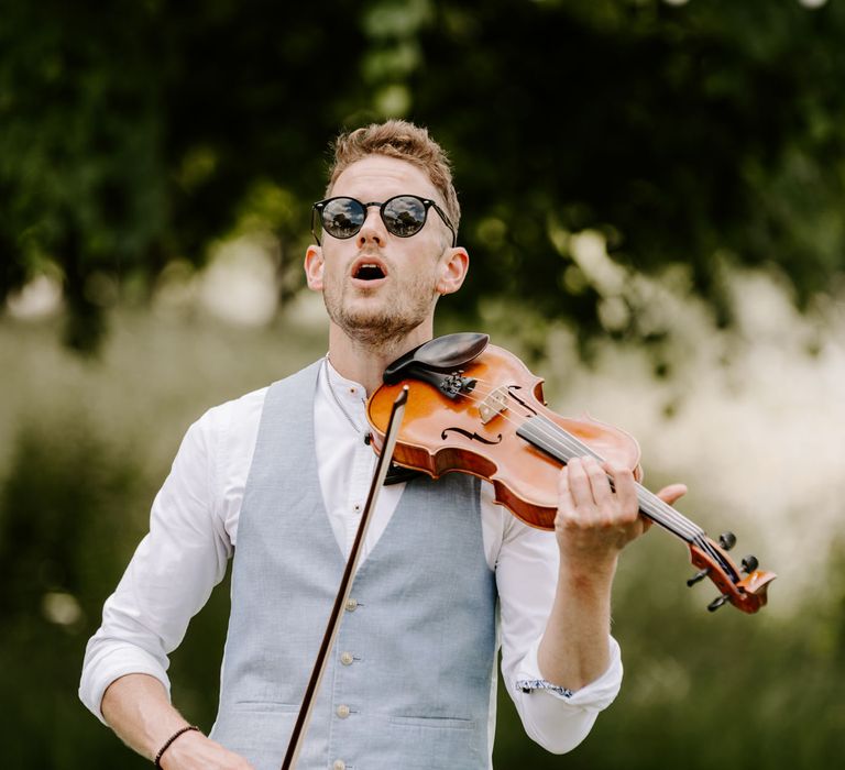 Violinist wears pale blue waistcoat as he plays violin outdoors on wedding day