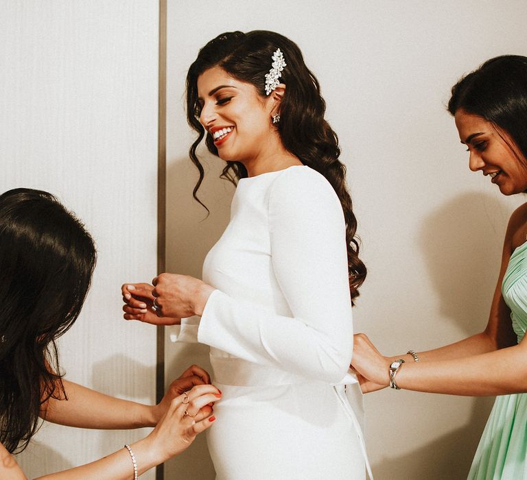 Bridesmaids in pastel dresses helping the bride into her wedding dress on the wedding morning 