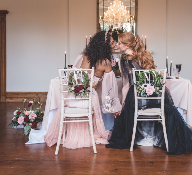 Two brides in coloured wedding dresses kissing at their intimate wedding reception at Thicket Priory