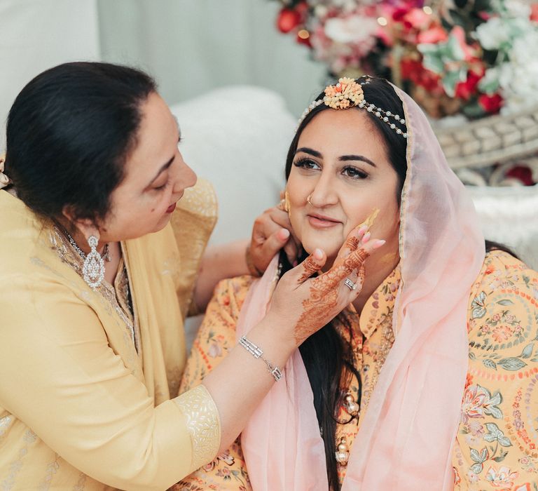 Bride during traditional Haldi ceremony in as wedding guest applies turmeric paste to her face