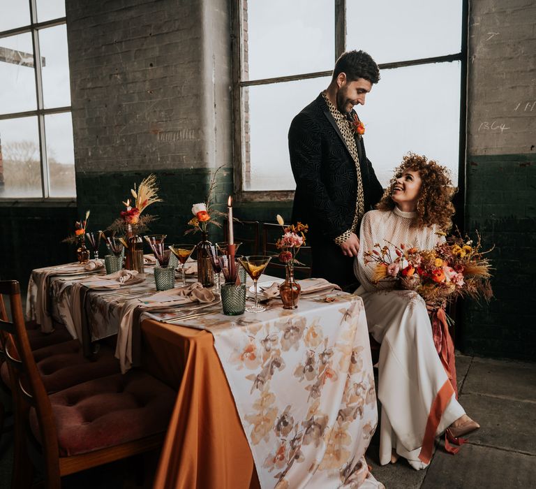 70s wedding inspiration at Atlas Studio in Manchester with bride in a jumpsuit, groom in a patterned shirt and brown and orange table decor 