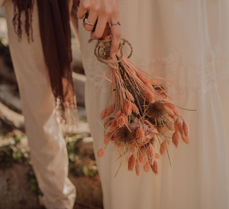 Bride holds dried floral bouquet with light pink hue and tied with thick brown string