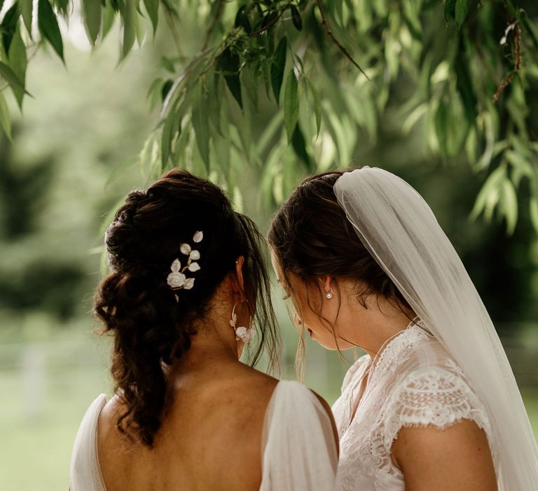 Bride with curled ponytail and leaf hair accessory stands with bride in lace capped sleeve wedding dress and veil in the grounds of The West Mill Derby after wedding ceremony