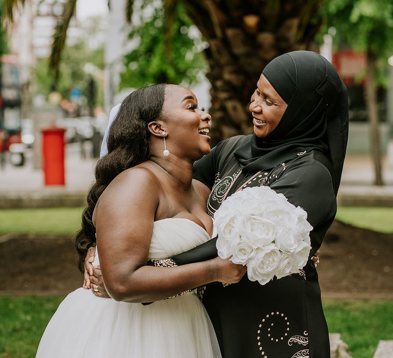 Bride looks lovingly at her mother whilst holding white bridal bouquet outdoors