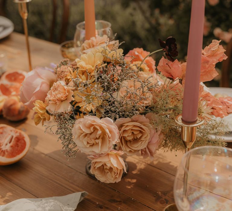 Pastel orange, peach, coral and yellow wedding flower arrangement at outdoor wedding reception 