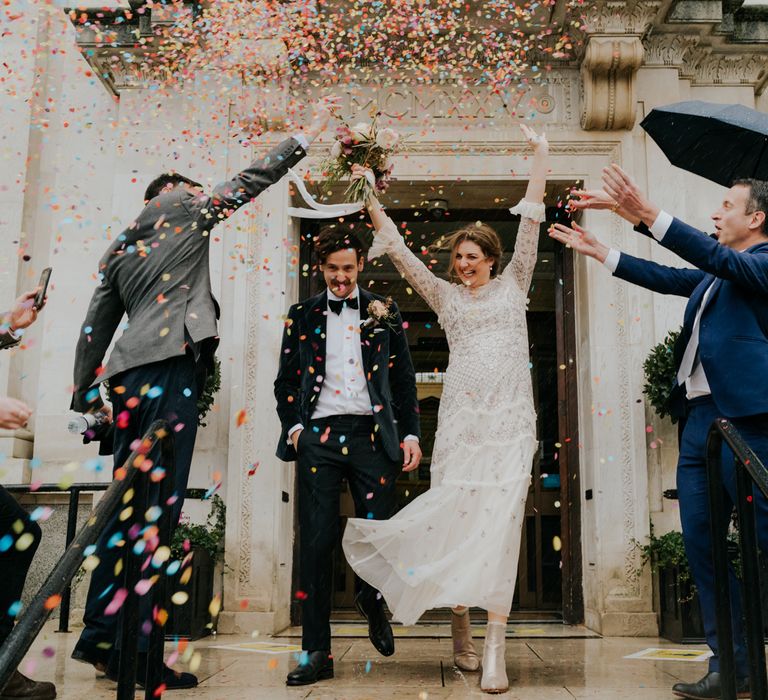 Bride & groom celebrate as wedding guests throw confetti around them after wedding ceremony 