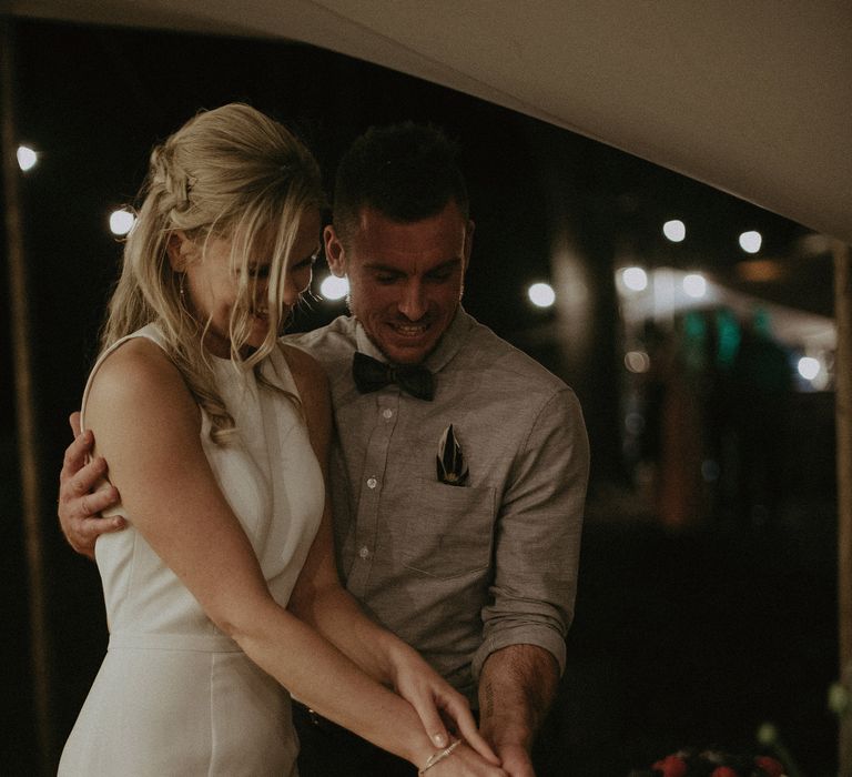 Bride & groom cut their wedding cake outdoors under tipi 