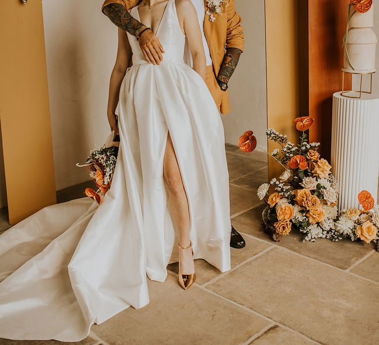 Bride in a Jesus Peiro wedding dress and groom in a mustard suit standing in front of orange and yellow geometric ceremony backdrops 