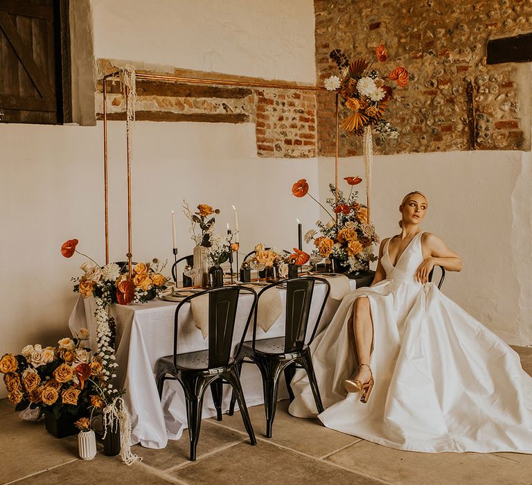 Bride in a Jesus Peiro wedding dress with V neck, long train and front split sitting at her black, orange, yellow and gold wedding table 