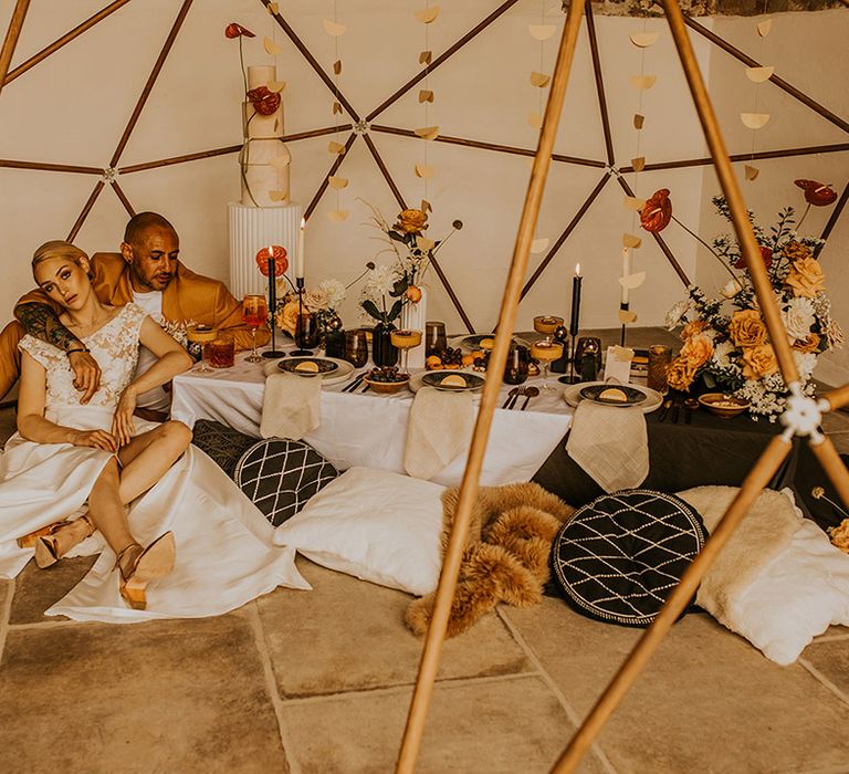 Intimate wedding reception under a wooden geodome structure with bride in a Jesus Peiro wedding dress and groom in a mustard suit 