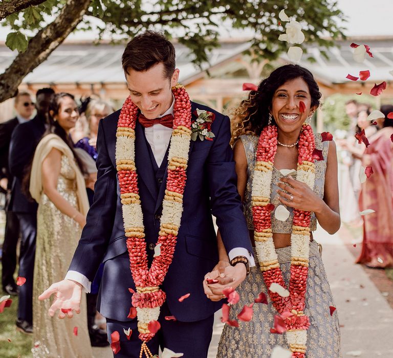 Bride & groom walk down the aisle wearing colourful garlands around their neck | Joshua Gooding Photography