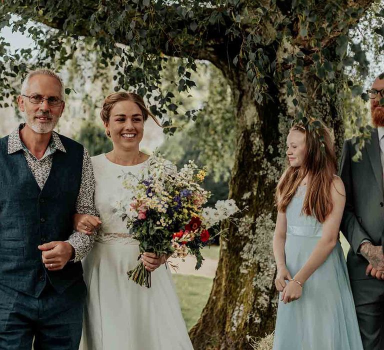 Bride walks down he aisle carrying wildflower bouquet