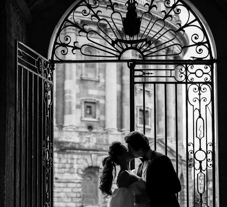 Black and white portrait of the stylish bride and groom kissing in the courtyard at Bodleian Library 