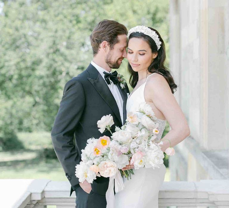 Groom in a tuxedo and bride in an appliqué headband holding a summer wedding bouquet with roses, peonies, icelandic poppies, sweet peas, scabious, foxglove, and snapdragons