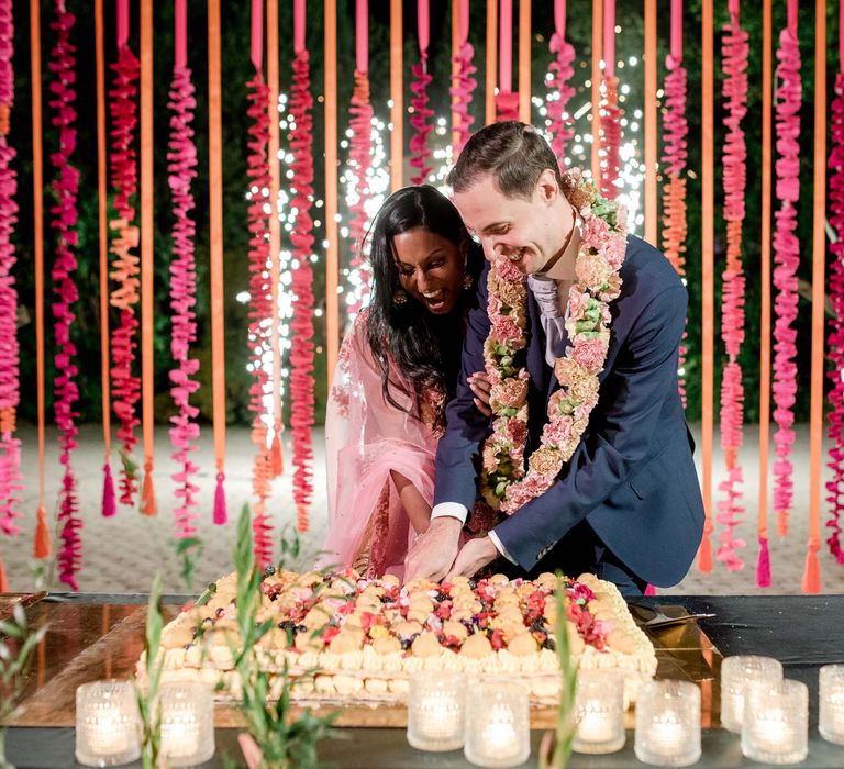 Couple cut their wedding cake in front of colourful hangings for hot pink and orange decor 