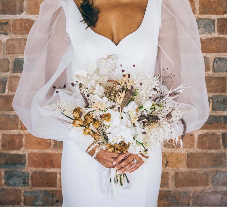 Beautiful bride in a sheer long sleeve wedding dress holding a dried flower bouquet with side braid and flower headband 