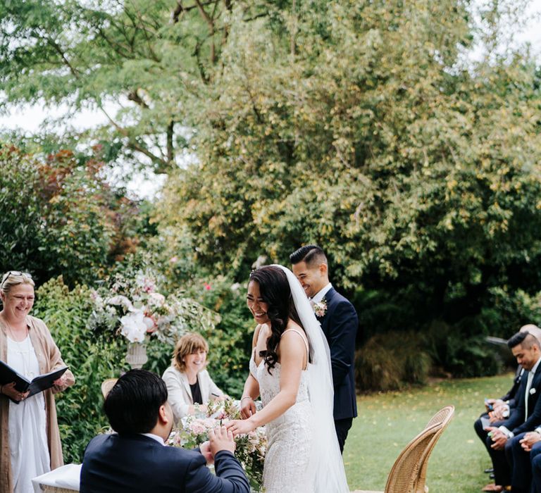 South Asian bride and groom smiling in outdoor ceremony in a navy suit and grey waistcoat and embellished wedding dress