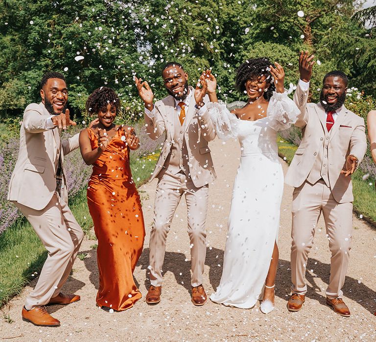 Wedding party confetti photograph with orange satin bridesmaid dresses, beige groomsmen suits and strapless wedding dress 