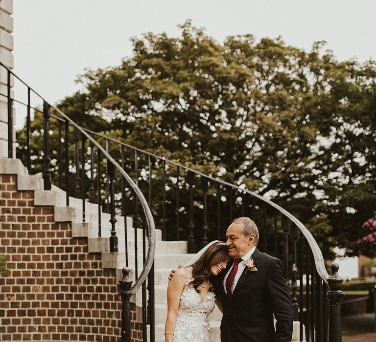 Bride leans her head into fathers shoulder on her wedding day as he wraps his arm around her