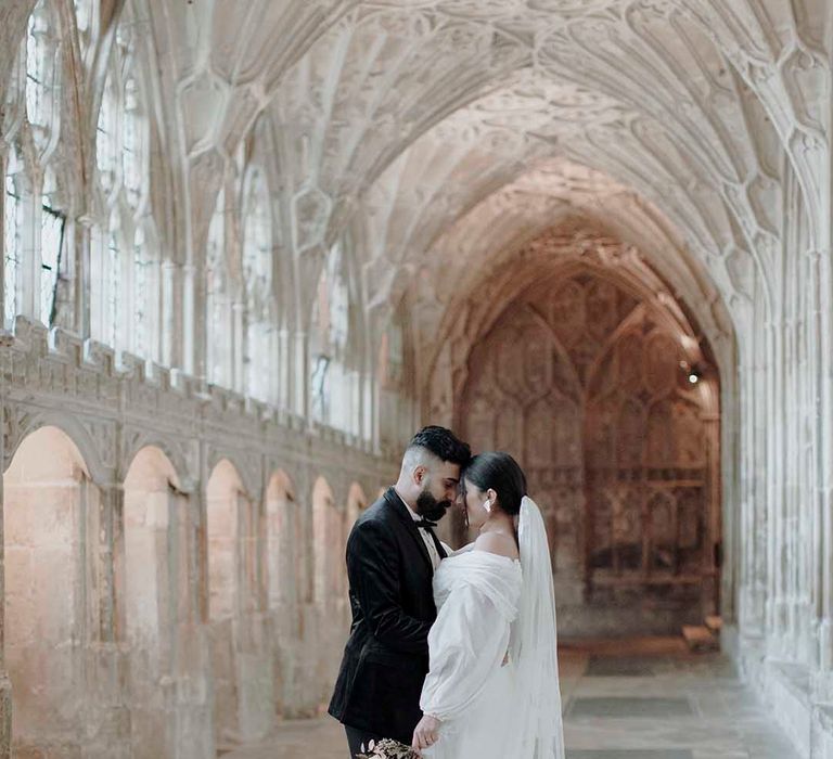 Portrait of the groom in a tuxedo and his bride in an off the shoulder wedding dress and lace embroidered cathedral length veil at the Blackfriars Priory 