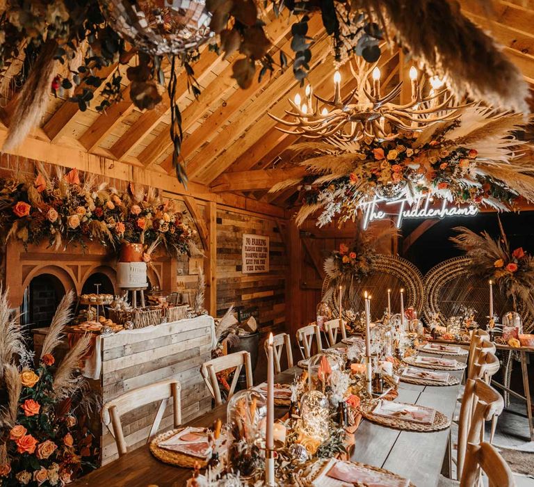 Boho barn wedding reception with autumnal florals, wooden table and chairs, candles, neon sign and disco balls at Kinmount House in Scotland