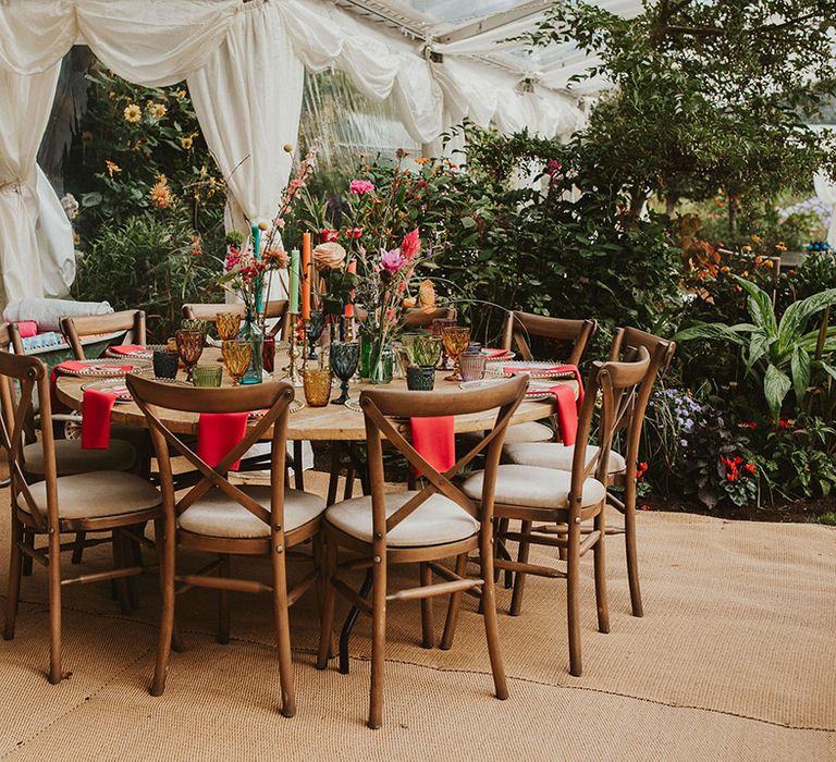 back garden wedding in a clear marquee with round wooden tables decorated with colourful linen, candles and flowers 