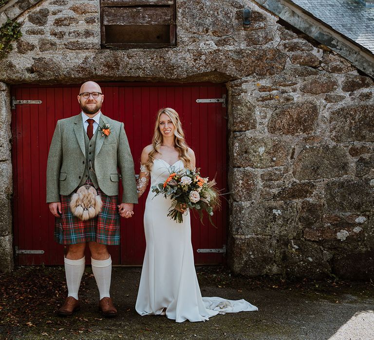 Bride & groom stand in front of red door on their wedding day