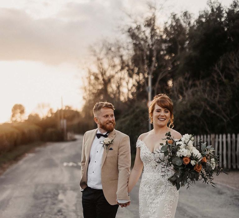 Bride in off the shoulder lace wedding dress with train and groom in beige coloured suit jacket