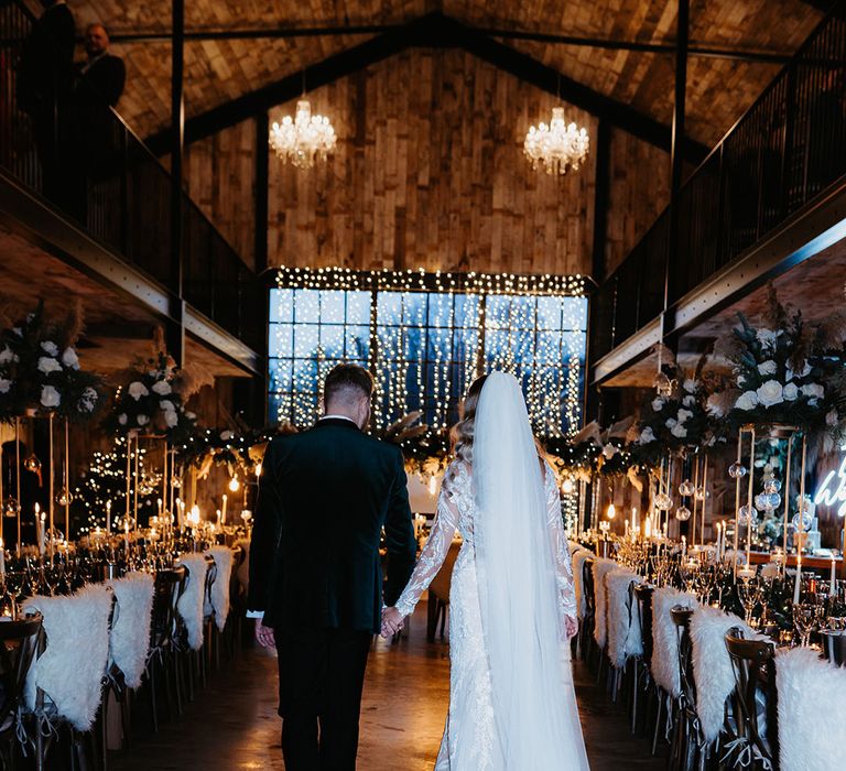 Bride and groom enter fairy lights wedding reception with fur details, white candles and other festive touches for Christmas wedding 