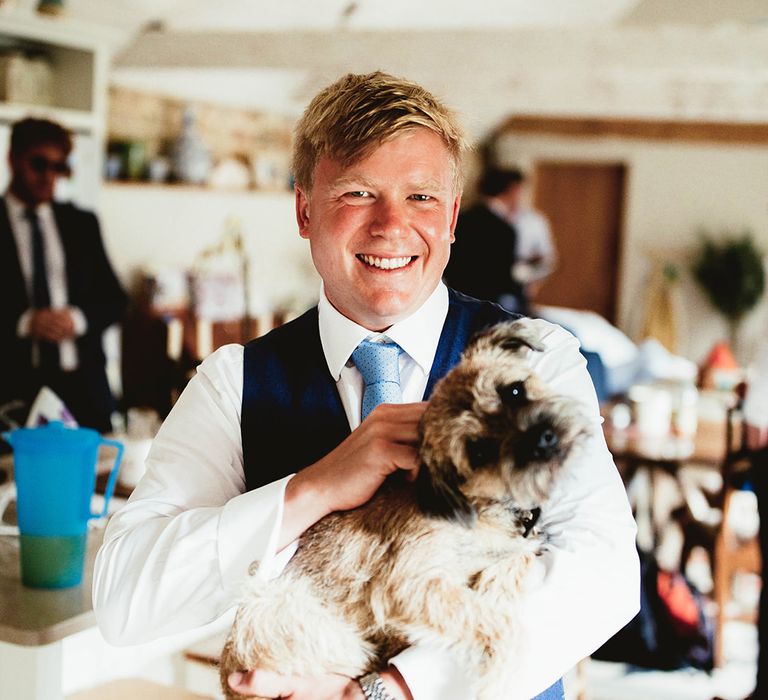 Groom gives pets to dog at wedding in blue waistcoat and white shirt