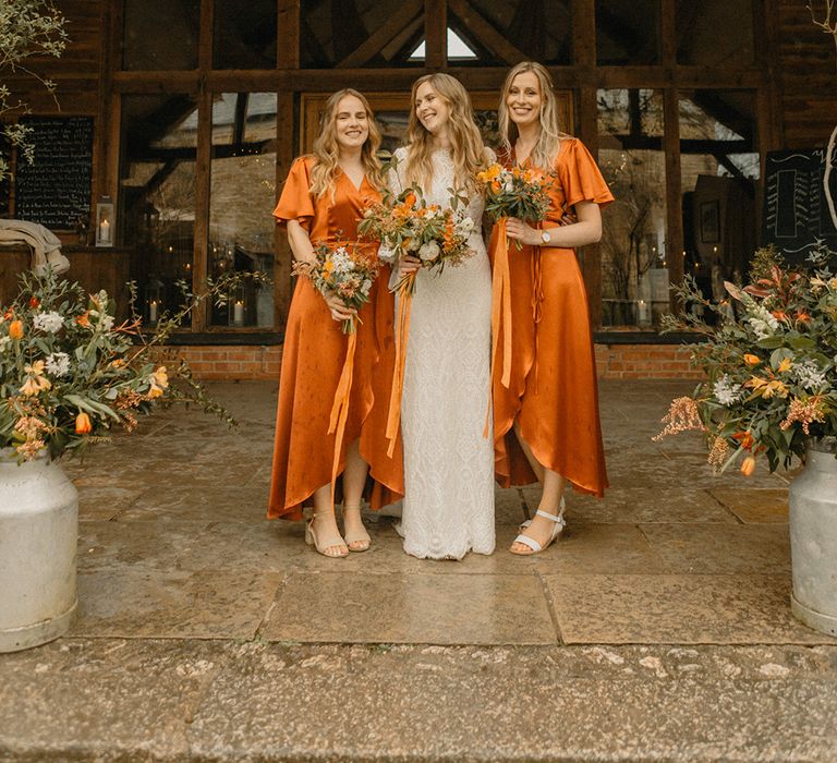 Bride in lace wedding dress with bell sleeves and bridesmaids with burnt orange satin wrap dresses