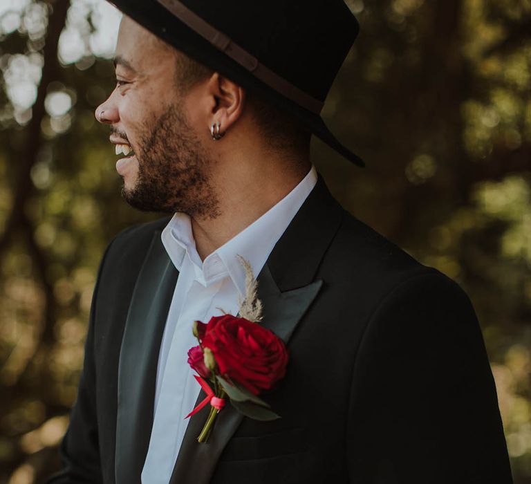 Groom in a black suit jacket with satin lapel, red buttonhole flower and open collar white shirt at Prestwold Hall wedding 