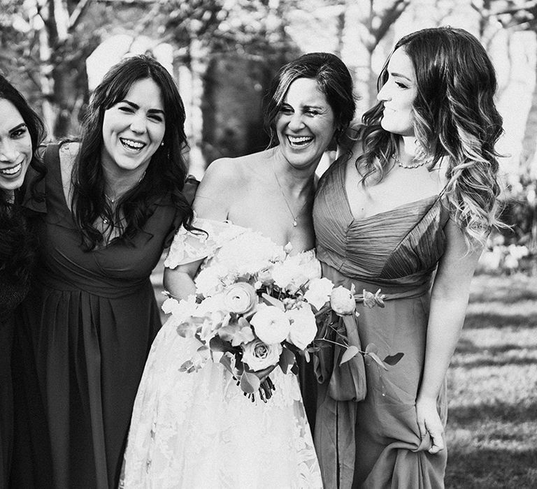 Bride in lace floral off the shoulder wedding dress laughs and smiles with bridesmaids