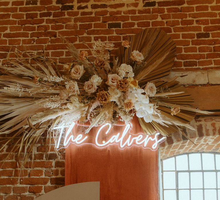 Dried flower wedding display with toffee and rust roses and personalised neon sign with the couples new name and cream signs