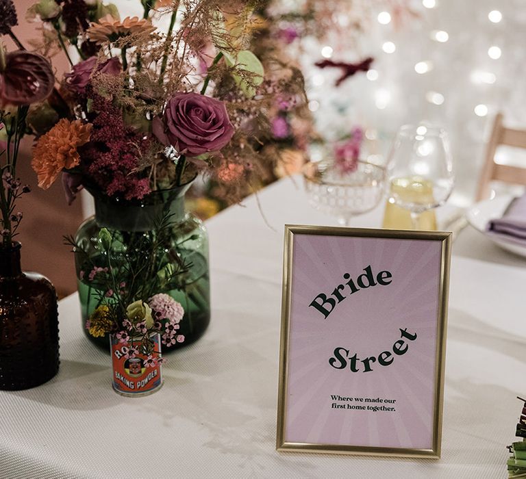 Purple table name sign in gold photo frame on tables with white tablecloths and lilac napkins