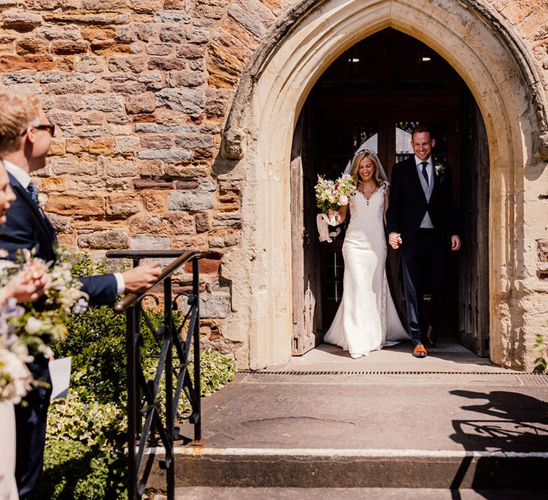 Bride and groom walk with intertwined hands out of their church wedding ceremony together 