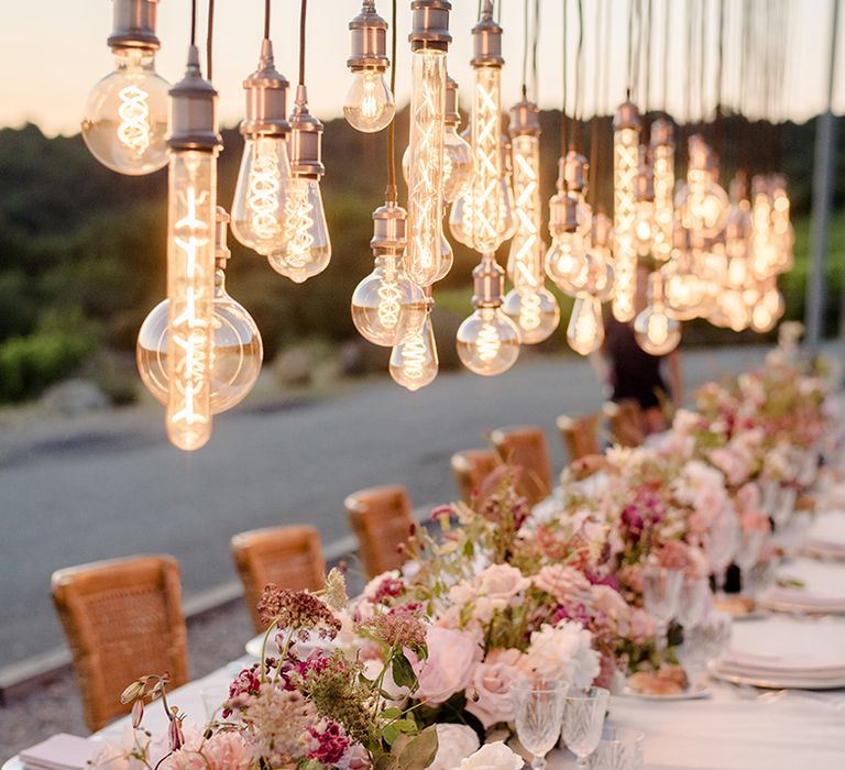 Decorative Edison bulbs installation hangs above head table outdoors in the Tuscan countryside 