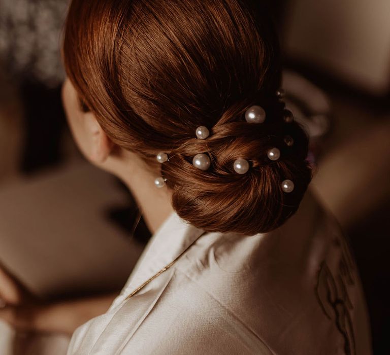 Bride wears her red hair in chignon bun complete with pearl hair accessories 