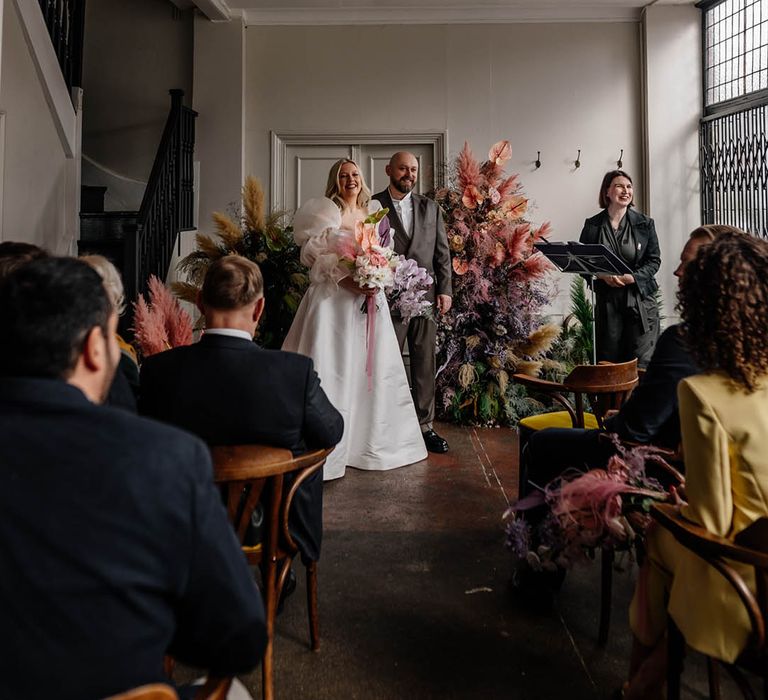 Floral Hall humanist wedding ceremony with column flowers at the altar, bride in a JESUS PEIRO wedding dress and groom a double breasted jacket