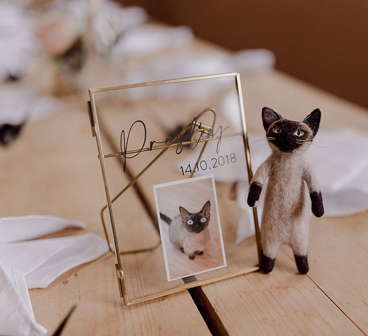 Miniature cat statue beside gold framed image of cat on wooden table