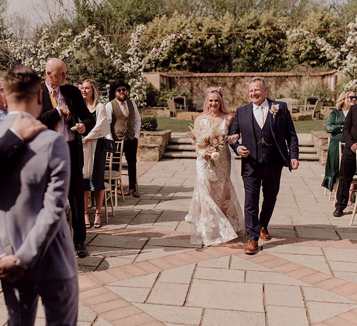 Bride wearing Jane Hill wedding dress walks down the aisle at Oxleaze Barn with her father for outdoor wedding ceremony